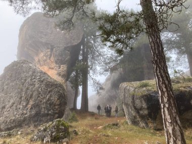 Cuenca, İspanya; 7 Aralık 2021: İspanya 'nın Castille La Mancha kentindeki kayalık oluşum ve ağaçlarla çevrili sisli bir arazide yürüyen yürüyüşçüler