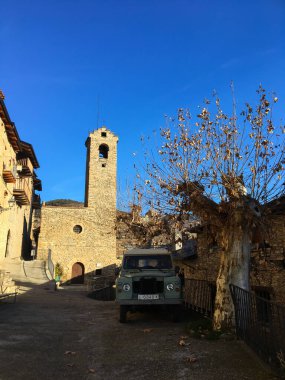 Estamariu, İspanya; 12 Aralık 2018: Katalonya 'nın Estamariu kentinde geleneksel taş kilise çan kulesinin yanına park edilmiş eski bir off road aracı
