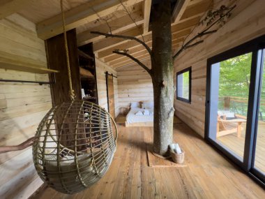 La Vall de Bianya, İspanya; 26 Ekim 2022: Ağaç gövdesi, asılı sandalye, yatak ve balkon erişimi olan ağaç ev içi