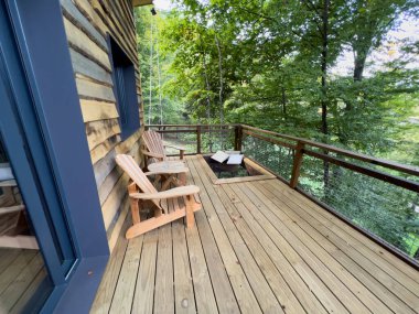 La Vall de Bianya, İspanya; 26 Ekim 2022: Adirondack sandalyeli kırsal ağaç ev güvertesi huzurlu bir orman inzivası sağlıyor