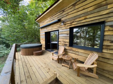 La Vall de Bianya, İspanya; 26 Ekim 2022: Doğayla çevrili bir jakuzi ve rahat sandalyeler içeren ahşap ağaç ev güvertesi