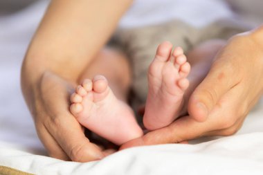 Annenin elleri yeni doğmuş bir bebeğin narin ayaklarını kucaklıyor. Sevgi ve ilgiyi simgeliyor.