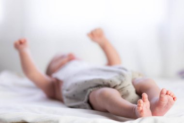 Küçük yeni doğmuş bebek beyaz bir masanın üzerinde ellerini ve ayaklarını esnetiyor.