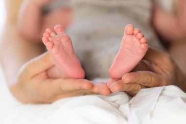 Ebeveyn elleri yeni doğmuş bir bebeğin küçük pembe ayaklarını nazikçe kucaklıyor. Sevgi ve ilgiyi simgeliyor.