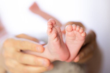 Ebeveynlerin elleri iki haftalık bir bebeğin küçük, yumuşak ayaklarını nazikçe tutuyor.