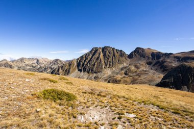 Pireneler, kuru sonbahar çimenleri ve canlı mavi bir gökyüzünün altındaki kayalık tepelerle kaplı dağlar.