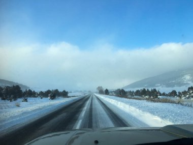 Karla kaplı manzaralı ve uzak dağlarla kısmen açık bir kış yolunda giden bir araç.