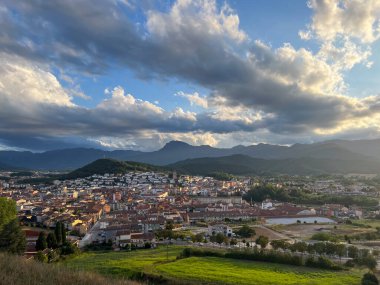 Olot şehri manzarası. Gün batımında binalar ve dağlar. Sıcak ışıkla aydınlanan bulutlar.