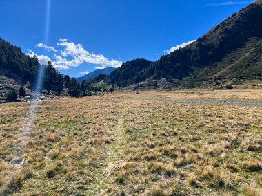 Geniş vadi tabanı kuru otlarla kaplı, dağlarla çevrili ve sonbahar gökyüzü