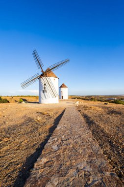 Mavi gökyüzünün altında kurak bir arazide duran yel değirmenleri kırsal mirası ve seyahati temsil ediyor.