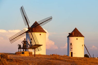 Günbatımında Don Kişot anıtı olan bir tepede duran tarihi İspanyol yel değirmenleri.