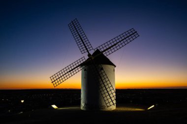 Yel değirmeni, gün batımının parlak gökyüzüne karşı duruyor, sıcak ışıkla aydınlanıyor.
