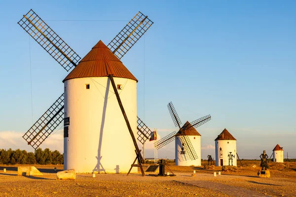 Açık mavi gökyüzünün altındaki kuru arazide duran yel değirmenleri, uzun gölgeler oluşturuyor.