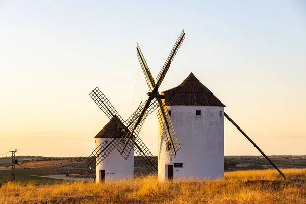 İki tarihi yel değirmeni, altın bir tepenin üzerinde, sıcak bir günbatımı gökyüzüne karşı görkemli bir şekilde duruyor.
