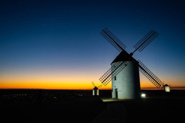 İspanya 'nın Mota del Cuervo şehrinde gün batımının renkli gökyüzüne karşı duran yel değirmenleri.