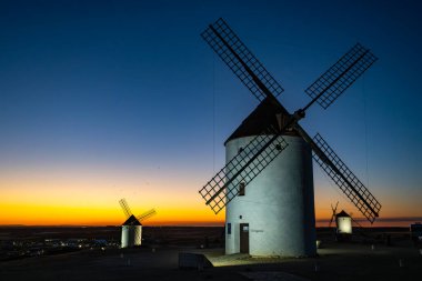 Yel değirmenleri İspanya 'nın Mota del Cuervo kentindeki bir tepede duruyor. Alacakaranlıkta turuncu ve mavi bir gökyüzü var.