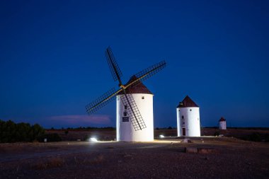 Tarihsel yel değirmenleri, La Mancha 'da alacakaranlıkta mavi gökyüzüne karşı aydınlandı.