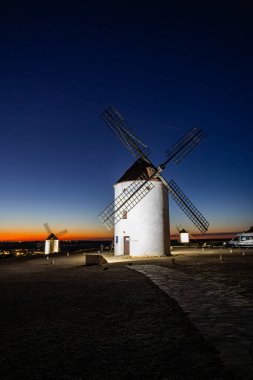 Akşam karanlığında tepelerde duran yel değirmenleri, tarihi bir İspanyol manzarası yaratıyor.