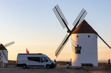 Altın saat boyunca tarihi bir İspanyol yel değirmeni sahasına park etmiş bir karavan, bir karavan hayat yolculuğu konseptini resmediyor.