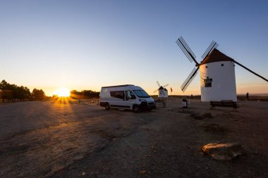 Altın saat boyunca bir tepenin tepesinde geleneksel yel değirmenlerinin yanına park edilmiş bir karavan.