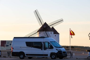 Campervan, İspanya 'nın La Mancha kentindeki Mota del Cuervo' da günbatımında tarihi yel değirmenlerinin yakınına park etti.