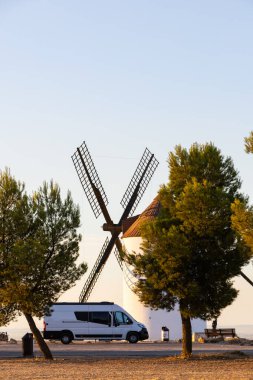 Gün batımında İspanya 'nın Mota del Cuervo kentindeki geleneksel yel değirmenlerinin yakınına park edilmiş bir karavan.