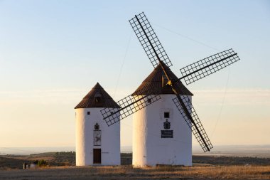 Geleneksel İspanyol yel değirmenleri açık gökyüzünün altındaki kırsal bir arazide bir tepenin üzerinde duruyorlar.