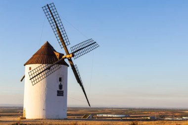İspanya La Mancha 'nın tarım manzarasını izleyen bir tepede duran yel değirmeni.