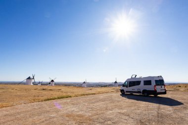 Kamp minibüsü Campo de Criptana, İspanya 'da güneşli bir gökyüzünün altında geleneksel yel değirmenlerine bakan bir tepeye park edilmiş.