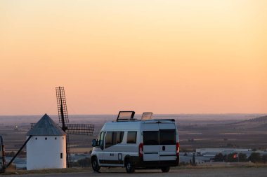 Gün batımında tepede klasik bir İspanyol yel değirmeninin yanına park edilmiş bir karavan.