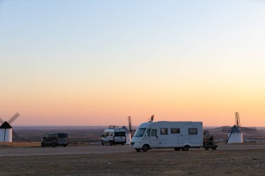 Campo de Criptana, İspanya 'da gün batımında tarihi yel değirmenlerinin yakınına park edilmiş eğlence araçları.