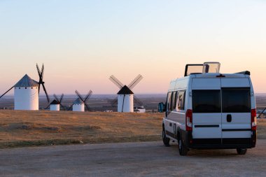 Gün batımında geleneksel İspanyol yel değirmenlerine bakan bir tepeye park edilmiş bir karavan.