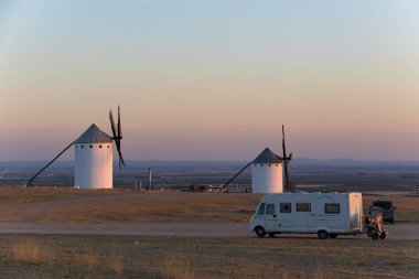 Altın tarlaya park etmiş bir karavan günbatımında geleneksel İspanyol yel değirmenlerine hayran.