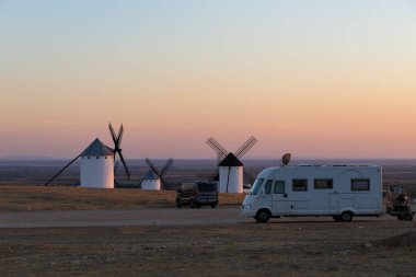 İspanya, La Mancha 'da gün batımında geleneksel yel değirmenleriyle birlikte bir tepeye park edilmiş bir karavan.