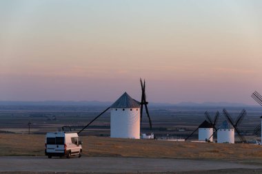 İspanya kırsalında gün batımında tarihi yel değirmenlerine bakan bir karavan park etmiş.