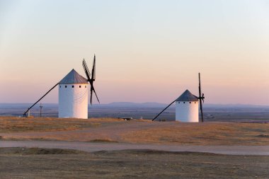 İspanya 'nın La Mancha şehrinde günbatımı gökyüzünün altındaki bir tepeye altın ışığı yansıtan tarihi yel değirmenleri.