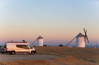 İspanya 'da gün batımını yansıtan yel değirmenleriyle dolu bir ovaya park edilmiş bir karavan.