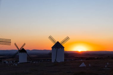 Geleneksel İspanyol yel değirmenleri La Mancha manzarasının üzerinde canlı bir gün batımına karşı duruyorlar.
