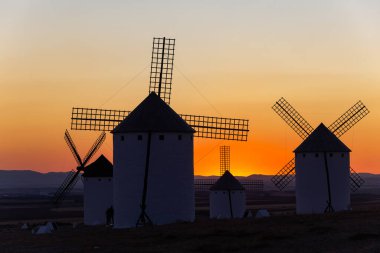 La Mancha kırsalının üzerinde canlı bir günbatımına karşı duran tarihi yel değirmenleri