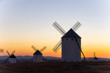 Geleneksel İspanyol yel değirmenleri, alacakaranlıkta güzel bir turuncu ve mavi gökyüzüne karşı dururlar.
