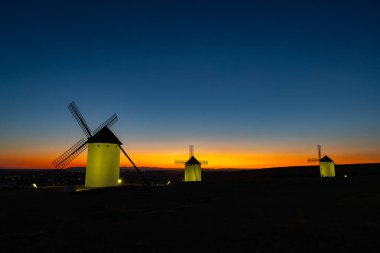 Tarihsel yel değirmenleri İspanya 'nın kırsal kesimlerinde turuncu ve mavi bir günbatımına karşı dururlar.