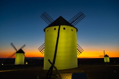 Alacakaranlıkta aydınlanan yel değirmenleri La Mancha 'da canlı turuncu ve mavi bir gökyüzüne karşı