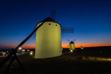 Alacakaranlıkta tepede duran yel değirmenleri, sıcak ve serin renkler gösteren gökyüzü