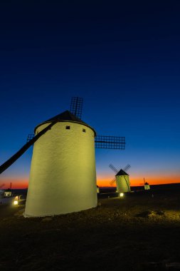 Alacakaranlıkta aydınlanan yel değirmenleri La Mancha 'da canlı mavi ve turuncu bir gökyüzüne karşı