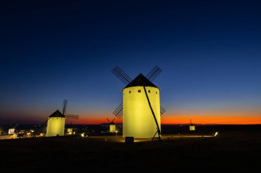 Campo de Criptana 'daki bir tepenin üzerinde duran aydınlık yel değirmenleri... alacakaranlıkta renkli bir gökyüzüyle...