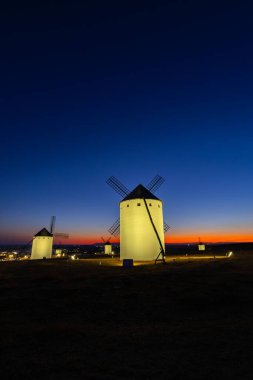 İspanya 'nın La Mancha şehrinde alacakaranlık saatlerinde bir tepenin üzerinde duran aydınlık yel değirmenleri