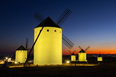 Geleneksel İspanyol yel değirmenleri, La Mancha 'da renkli bir alacakaranlık gökyüzüne karşı aydınlanıyor.