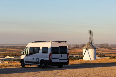İspanyol kırsalında altın saatinde geleneksel bir yel değirmeninin yakınına park edilmiş bir karavan.