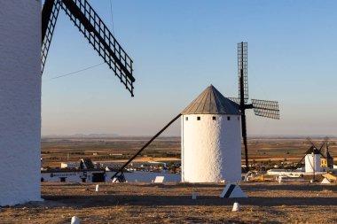 Kuru bir tepede beyaz yel değirmenleri ovalara bakan ve temiz bir gökyüzünün altındaki bir kasaba