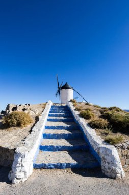 Geleneksel İspanyol yel değirmeni, açık mavi gökyüzünün altındaki tepeden manzaraya bakıyor.